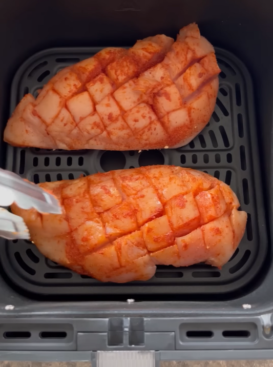 Kreuzweise eingeschnittene und gewürzte Hähnchenbrustfilets im Airfryer-Korb