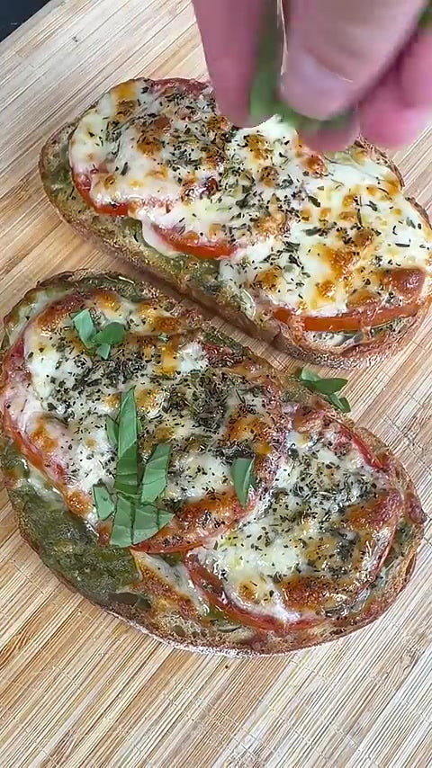 Zwei Caprese-Toasts mit geschmolzenem Mozzarella, Tomaten, Pesto und Basilikum auf einem Brett