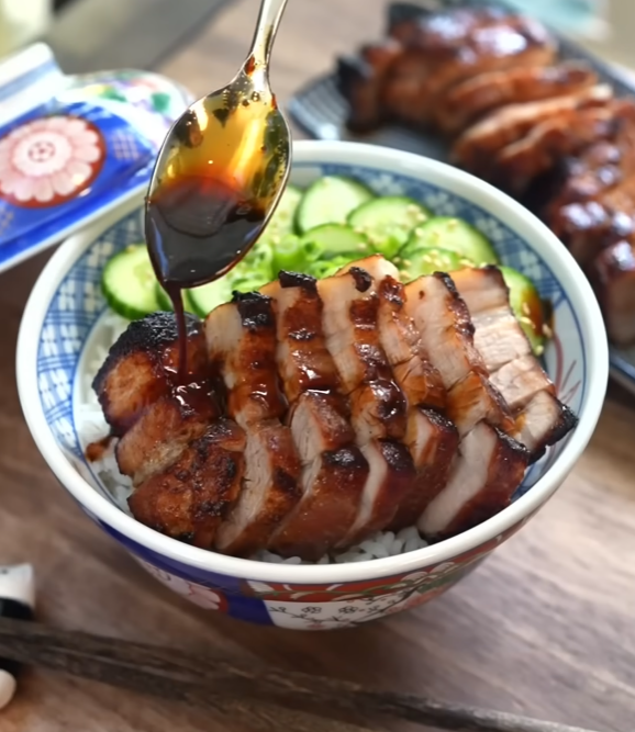 Aufgeschnittener honigglasierter Schweinebauch mit Reis und Gurke